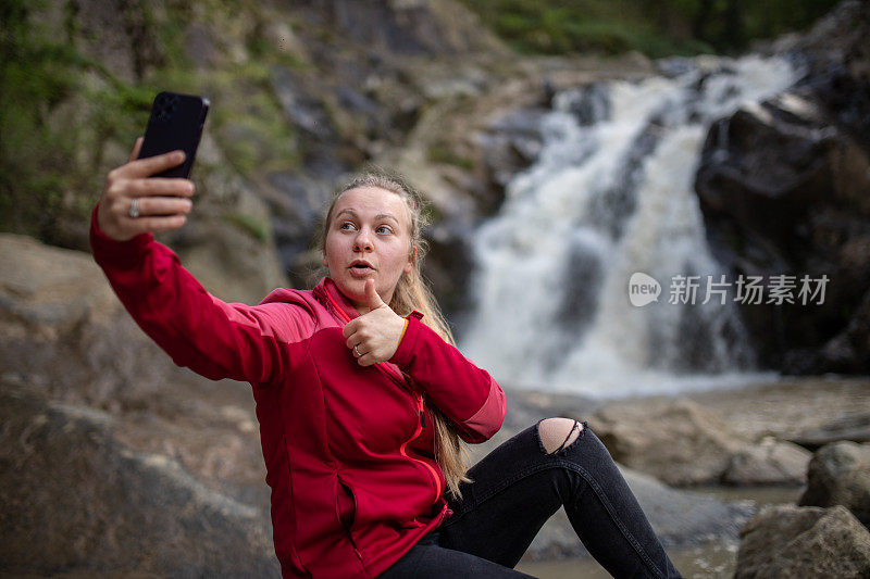 年轻的徒步旅行者在大自然中用她的智能手机为她的粉丝打视频电话/录制视频